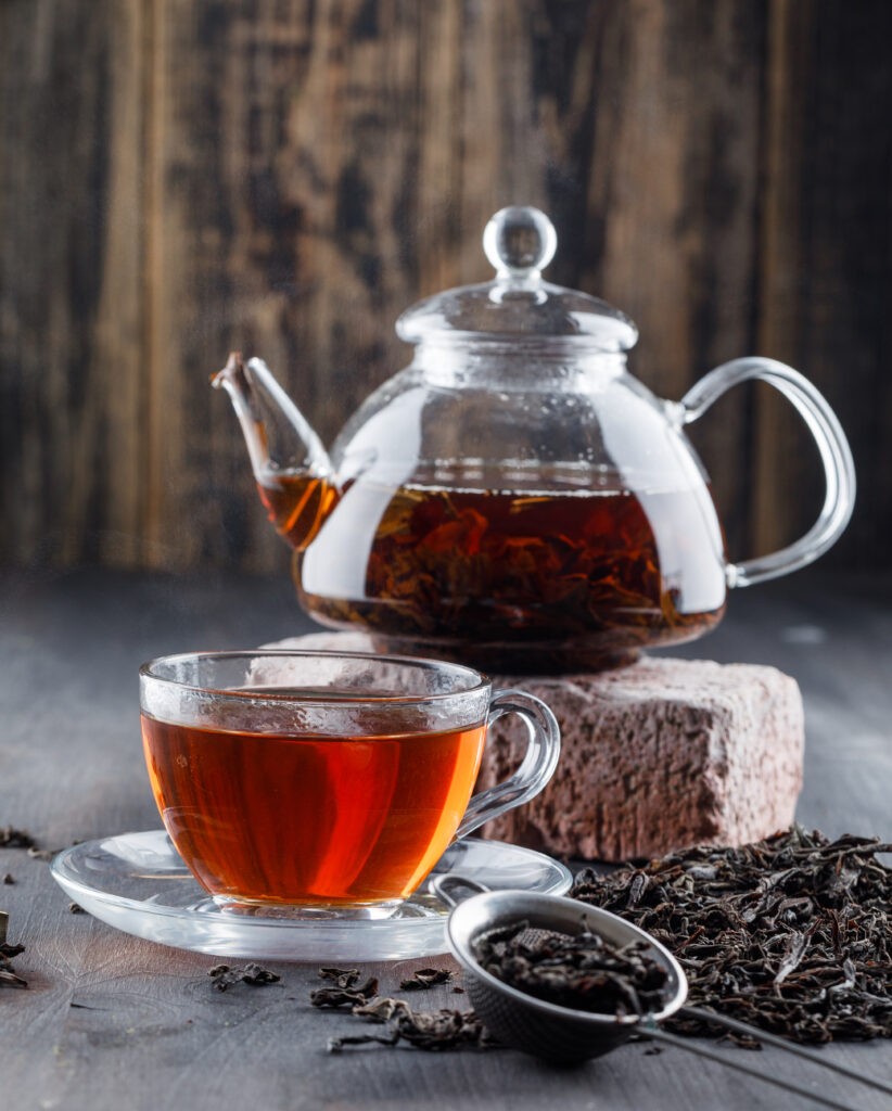 black tea in teapot and cup with dry tea, brick side view on a wooden background